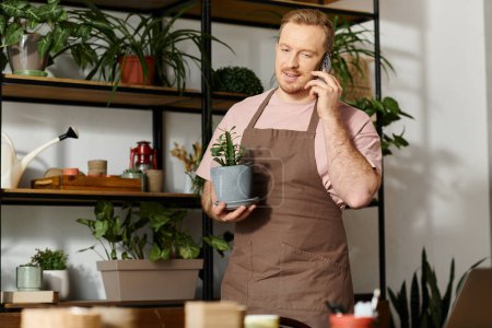 Un hombre multitarea, sosteniendo una planta en maceta y hablando en un teléfono celular en una tienda de plantas.