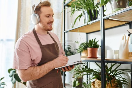 Foto de Un hombre con auriculares se para frente a un estante en una tienda de plantas, inmerso en su propio mundo. - Imagen libre de derechos