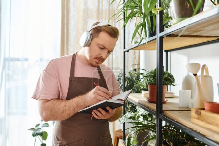 A man in an apron and headphones takes notes on a clipboard in a vibrant plant shop, embodying a dedicated small business owner.