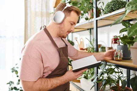 A man wearing headphones is attentively looking at a notebook in a plant shop, reflecting on the beauty of nature.