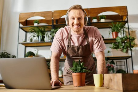 A man with headphones sits in front of a laptop, immersed in his work, at a plant shop. He exudes focus and creativity.