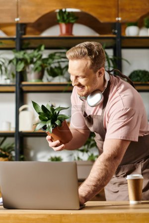Foto de Un hombre con auriculares deportivos se concentra en su portátil, inmerso en la gestión de las operaciones de sus tiendas de plantas. - Imagen libre de derechos