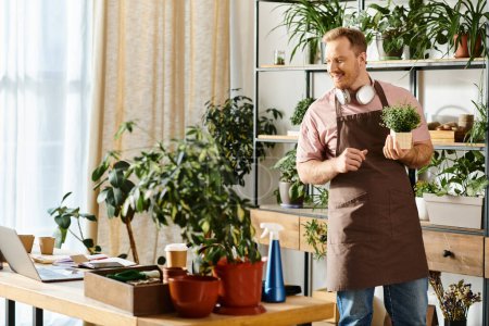 A handsome man in an apron proudly holds a potted plant in a plant shop, showcasing his love for greenery.
