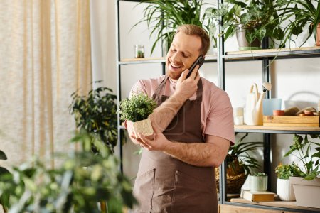 Ein stylischer Mann, der mit einem Handy spricht, während er in einem Pflanzenladen eine Topfpflanze in der Hand hält.