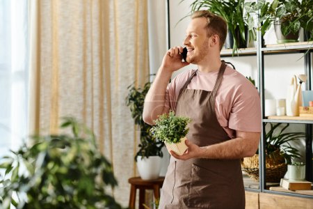 A man chatting on cell phone and holding a potted plant in a plant shop, embodying multitasking and business ownership.