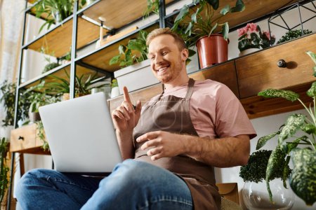 Un homme s'assoit sur le sol à l'aide d'un ordinateur portable dans un magasin d'usine, se concentrant sur sa petite entreprise et maintenant un fleuriste à succès.
