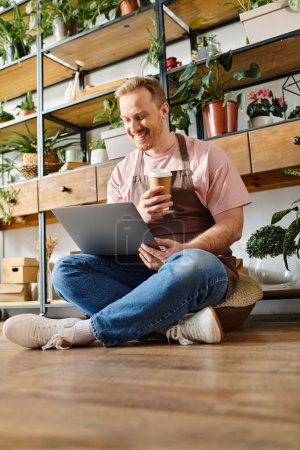 Ein Mann, der auf dem Boden sitzt, in seinem Laptop inmitten üppigen Grüns versunken, verkörpert das Wesen eines modernen Unternehmers.