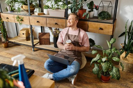 A man peacefully sits on the floor, cradling a cup of coffee in a cozy plant shop setting.