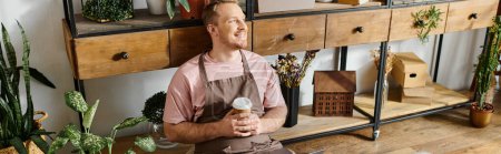 Foto de Un hombre elegante está junto a un estante, sosteniendo una taza de café en una tienda llena de plantas. - Imagen libre de derechos