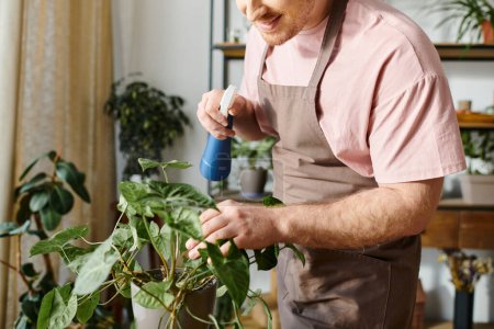 A man in an apron is carefully spraying a potted plant in a plant shop, showcasing his expertise in gardening.