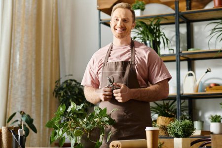 Foto de Un hombre guapo está en su tienda de plantas, rodeado de vegetación y varias plantas en maceta en una mesa. - Imagen libre de derechos