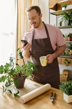 Man in apron holding cup, checking phone in small plant shop. Business owner multitasking during busy day.