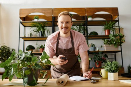 A man in an apron holds a cell phone in a plant shop setting.