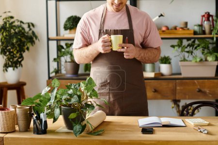 Téléchargez les photos : Un homme dans un tablier dégustant une tasse de café dans un cadre de magasin de plantes, prenant un moment pour se détendre et savourer la boisson chaude. - en image libre de droit
