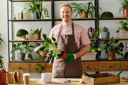 Un hombre guapo en un delantal sosteniendo una planta en maceta en una tienda de plantas, mostrando la belleza de ser dueño de una pequeña empresa.