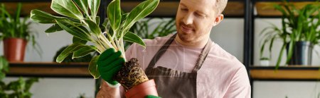 Un hombre delicadamente sostiene una planta en maceta en sus manos, rodeado de exuberante vegetación en una tienda de plantas.