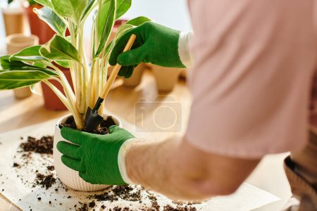 Une personne en gants verts met délicatement en pot une plante avec un sol riche dans un cadre de fleuriste de petite entreprise.
