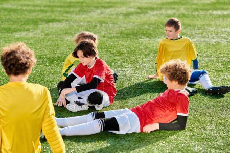 A group of young children sits atop a vibrant green soccer field, chatting and laughing. They seem eager and excited, perhaps planning their next game or just enjoying each others company under the blue sky.