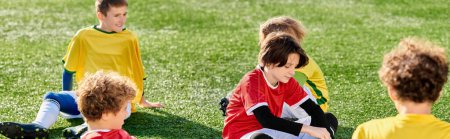 A group of young children, full of energy and enthusiasm, sit atop a lush green soccer field. They are engaged in conversation, laughter, and camaraderie, creating a joyful atmosphere.
