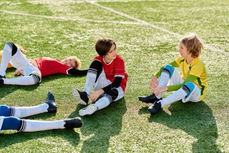 A group of young children gleefully sit atop a vibrant soccer field, chatting and laughing. Their bright energy and playful spirit fill the space with pure joy and excitement.