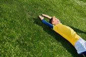 A young boy in a soccer uniform lies peacefully on the grass, staring at the sky with a smile on his face, lost in thoughts of the beautiful game. t-shirt #707501500