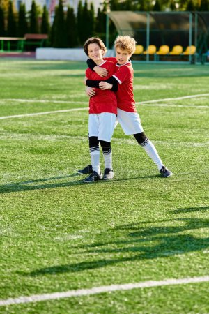 Two young boys, wearing soccer gear, lovingly hug each other on the green soccer field. Their faces radiate happiness and sportsmanship as they celebrate together.