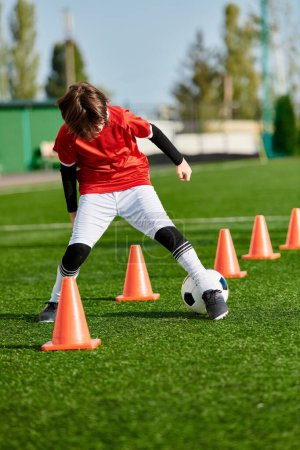 Ein talentierter kleiner Junge manövriert gekonnt einen Fußball um leuchtend orangefarbene Kegel auf einem Feld und zeigt dabei seine Beweglichkeit und Präzision im Dribbling und Kicken..