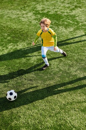 A young boy energetically kicks a soccer ball across a vibrant green field, displaying skill and determination in his game.