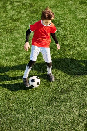 Ein kleiner Junge kickt energisch gegen einen Fußball auf der grünen Wiese. Seine Konzentration ist offensichtlich, wenn er seine Fähigkeiten trainiert und bei jedem Tritt auf Präzision und Kraft abzielt..