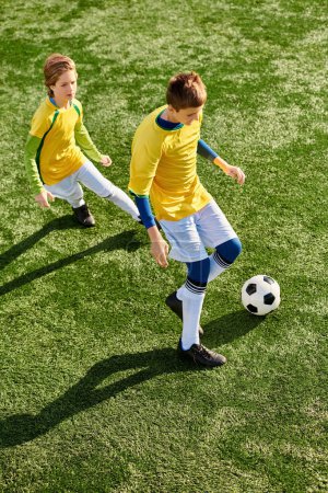 Two energetic young boys running on a vibrant green soccer field while kicking a soccer ball back and forth.