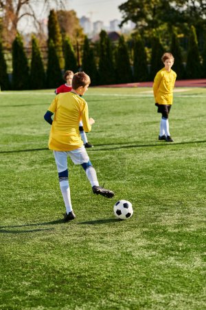 Téléchargez les photos : Un groupe de jeunes garçons jouant passionnément un jeu de football sur un terrain vert. Ils courent, donnent des coups de pied au ballon, et crient de joie pendant qu'ils rivalisent. - en image libre de droit