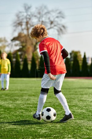 Foto de Un joven con una expresión determinada patea una pelota de fútbol en un campo verde exuberante bajo el sol brillante, mostrando su pasión por el juego. - Imagen libre de derechos