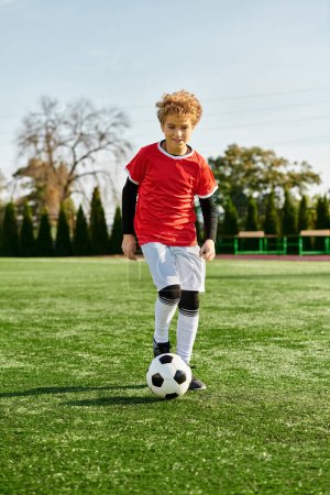 Photo for A young boy displaying his soccer skills by confidently kicking a soccer ball on a grassy field. His focus and determination shine through as he practices his technique on the pitch. - Royalty Free Image