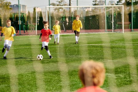 Grupa młodych mężczyzn zaangażowanych w uduchowioną grę w piłkę nożną na zielonym polu, goniąc za piłką, pokazując pracę zespołową, umiejętności i determinację podczas intensywnego meczu.