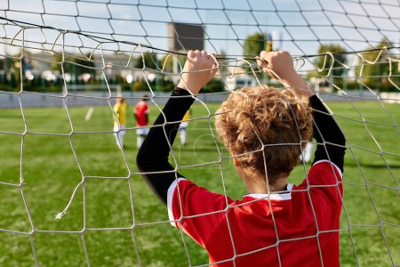 Un jeune garçon se tient en confiance devant un filet de football, prêt à se défendre contre tout tir entrant avec détermination et concentration.