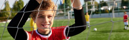 A young boy with a look of determination stands behind a soccer net. He is practicing his goalkeeping skills, ready to defend the goal with agility and precision.