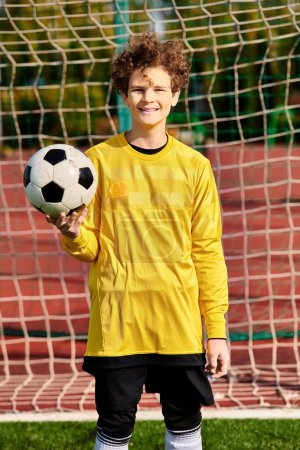 Un joven se para frente a un gol, sosteniendo una pelota de fútbol en sus manos, listo para disparar, con determinación en sus ojos.