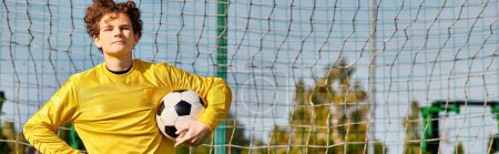 Ein junger Mann hält selbstbewusst einen Fußball vor ein Netz, bereit für einen Schuss. Die Vorfreude und Intensität des Augenblicks sind spürbar, während er sich auf das Ziel vorbereitet.