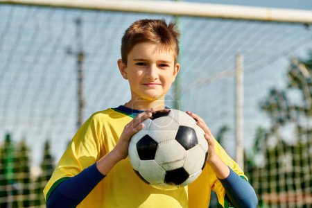 Un joven se para frente a un gol de fútbol, sosteniendo una pelota de fútbol en sus manos. Él mira hacia adelante con determinación, listo para disparar hacia la red.