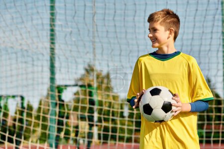 Téléchargez les photos : Un jeune garçon se tient en confiance devant un but, ballon de football à la main, envisageant sa victoire. Son regard est fixé sur le net, détermination dans ses yeux. - en image libre de droit