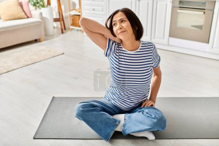 Foto de Mujer madura en ropa de casa acogedora practicando yoga en una estera en su sala de estar. - Imagen libre de derechos
