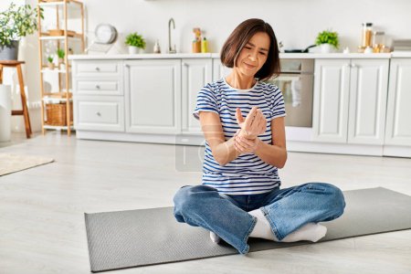 A mature beautiful woman in comfy homewear practices yoga on a kitchen mat.