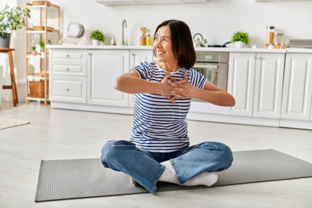 Une belle femme mature en tenue confortable pratique le yoga sur un tapis dans sa cuisine.