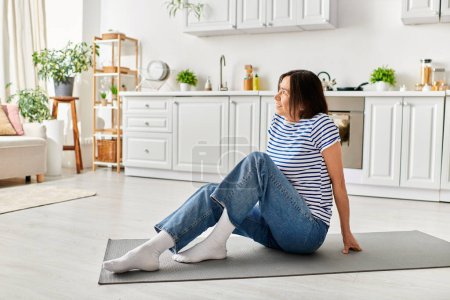Reife Frau in gemütlicher Hausbekleidung beim Yoga auf einer Matte in ihrem Wohnzimmer.