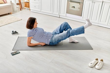 Reife Frau in gemütlicher Hauskleidung praktiziert Yoga auf einer Matte in ihrem Wohnzimmer.