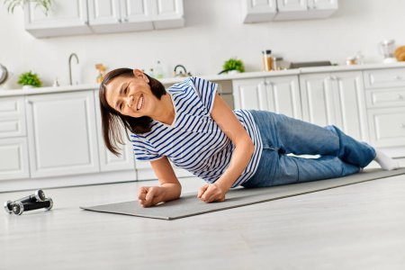 A mature beautiful woman in cozy homewear practices yoga on a mat in her kitchen.