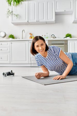 Téléchargez les photos : Une femme mature en tenue de maison pratique le yoga sur un tapis dans une cuisine ensoleillée. - en image libre de droit