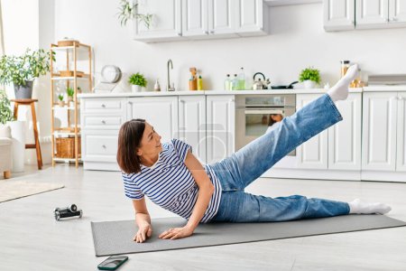 Reife Frau in gemütlicher Homewear macht Yoga auf einer Küchenmatte.
