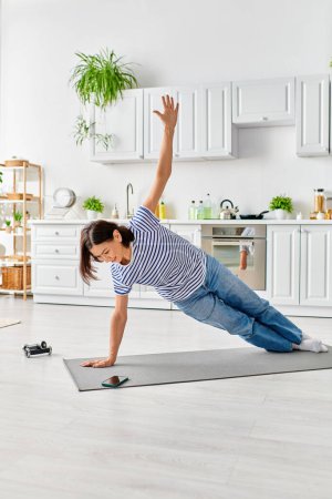 Reife Frau in gemütlicher Hauskleidung praktiziert Yoga-Pose auf Matte zu Hause.