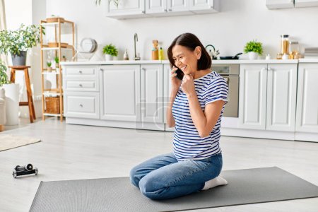Una mujer madura en ropa de casa chats en su teléfono mientras está sentada en una esterilla de yoga.